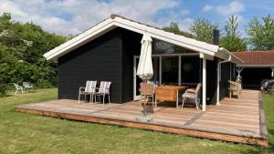 a black cabin with a deck and an umbrella at R963-Rodvig-Skovstumperne-3 in Rødvig