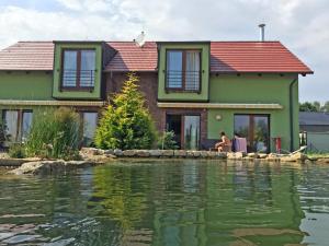 una donna seduta davanti a una casa vicino a uno specchio d'acqua di Lake View Apartments at Golf Resort Kunětická Hora, Dříteč a Bukovina
