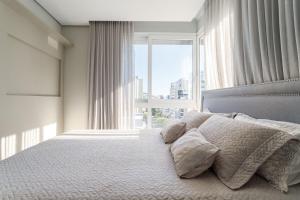 a bedroom with a bed with pillows and a large window at Apto 2 Quartos com Sacada Ed.Jardim Milano in Florianópolis +17 photos