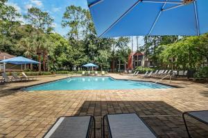 a swimming pool with an umbrella and chairs at Landing Apartments - Jacksonville in Jacksonville