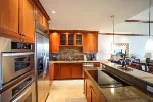 a kitchen with wooden cabinets and stainless steel appliances at Kolea 14F - Heated Pool Gym & More in Waikoloa