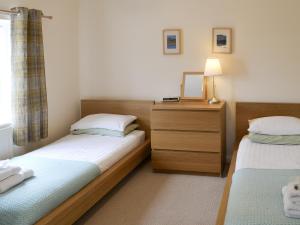 a bedroom with two beds and a dresser and a mirror at Teal Cottage in Embleton