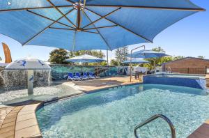 a swimming pool with a blue umbrella and chairs and a pool at Ingenia Holidays Hervey Bay in Hervey Bay