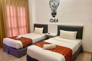 two beds in a hotel room with a sign on the wall at Hotel Dlima Inn Plaza Mahkota Melaka in Melaka