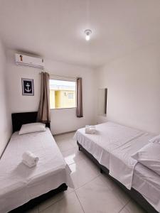 two beds in a white room with a window at Residencia Praia Dos Corais H100 in Santa Cruz Cabrália