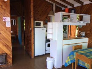 a small kitchen with a white refrigerator and a table at Cabaña Celeste - Acceso directo a playa lago Caburgua y cancha de tenis - direct access Beach in Caburgua Lake and tenis court in Pucón