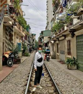 una donna che indossa una mascherina in piedi sui binari del treno di Tonkin1987 a Hanoi