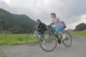 a man and a woman riding bikes down a road at guesthouse goma in Nantan city