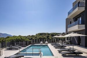 a swimming pool with chairs and umbrellas on a building at Heliodora Villa, Premium Nature Living, By ThinkVilla in Áyios Mámas