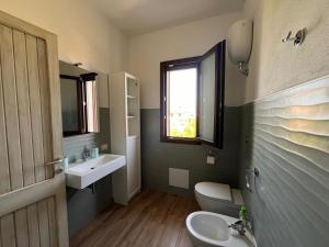 Un baño con lavabo, inodoro y ventana. en Porto Columbu, en Porto Columbu - Perdʼe Sali