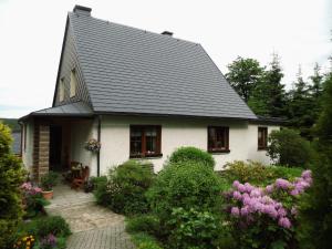 una casa blanca con techo gris y algunos arbustos en Ferienwohnung Ulbrich, en Schellerhau