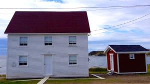 a house with a red roof next to a body of water at The Old Salt Box Co - Gertie's Place in Twillingate