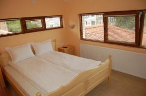 a bedroom with a bed with white sheets and windows at Къщи "И пак дойдох" in Tryavna