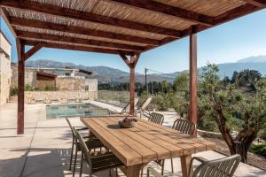a wooden table and chairs on a patio with a pool at Olive Hideaway Boutique Villa - Private Pool - 7 Pax -Pet Friendly in Kalamitsi Amygdali