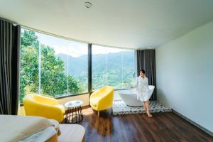 Una mujer parada en una habitación de hotel con bañera y una ventana grande. en Mây ơi homestay- Venuestay, en Sa Pa
