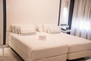 a white bed with two pillows and a sign on it at Hotel Málaga Nostrum Airport in Málaga