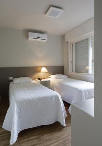 um quarto com 2 camas com lençóis brancos e uma janela em Apart Hotel Garibaldi em Porto Alegre
