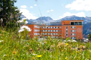an orange building with mountains in the background at Hotel Prätschli in Arosa