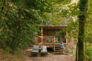 a woman sitting on the porch of a log cabin at Slow Village Anduze - Cévennes in Corbés