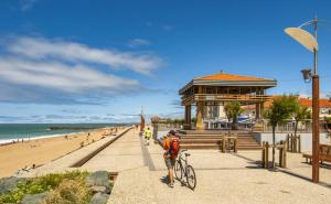 a man riding a bike on a sidewalk next to a beach at Appartement 2 ch Anglet Biarritz in Anglet