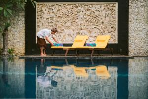 a man standing next to two chairs next to a swimming pool at The Casa Amaya in Jimbaran