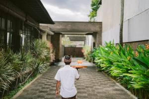 a man walking down a sidewalk carrying a table with drinks on it at The Casa Amaya in Jimbaran