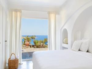 a white bedroom with a view of the ocean at Mykonos Lolita, a Resort to Live in Agios Sostis Mykonos
