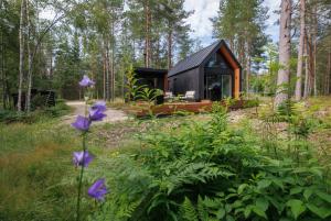 a black tiny house in the woods with purple flowers at Keibulahe Puhkemaja in Keibu