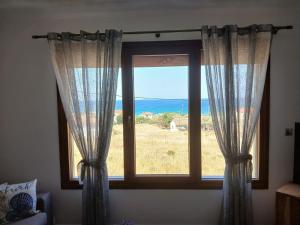 a window with curtains and a view of the ocean at Διαμέρισμα με θέα - Sunset House Lemnos in Agios Ioannis Kaspaka