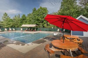a table with a red umbrella next to a pool at LilBear- AC, Pool, Sauna, Hot Tub, Near Resort in Killington