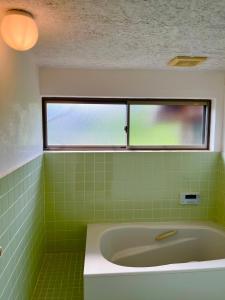 a green tiled bathroom with a tub and a window at 古民家ステイshinonome inn in Kitsuki +23 photos