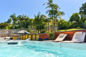 a swimming pool with lounge chairs and palm trees at La Maison Soleil - Waiheke Island in Waiheke Island