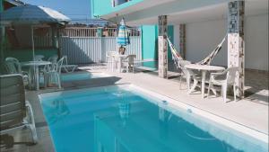 a swimming pool with chairs and tables and an umbrella at DaLua Suítes in Ubatuba