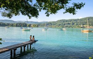 ペルトシャッハ・アム・ヴェルターゼーにあるFerienwohnung Pörtschach 52M²のボートのある水上の桟橋に座っている二人 +16枚の写真