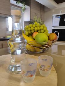 a bottle and three cups on a table with a bowl of fruit at The old Phone Center house in Ierápetra +6 photos