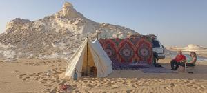 a tent in the desert with two people and a van at White Desert Soul Safari Camp Desert Experience in Mandīshah