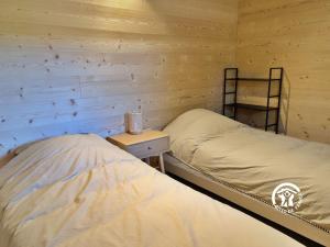 two beds in a room with wooden walls at Chalet 26 Le Berthevin, Camping de Coupeau, 4 personnes in Saint-Berthevin