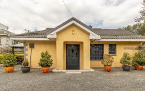 a yellow house with a black door and some plants at Bremu Home - Near jkia airport in Nairobi
