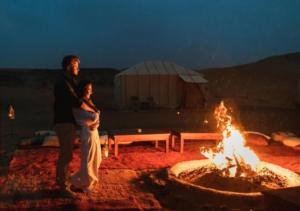 a man and a woman standing next to a fire at Sahara horizon Camp in Merzouga