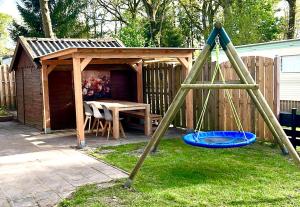 a wooden shed with a table and a playground at Huisje Eext - De Vos in Eext