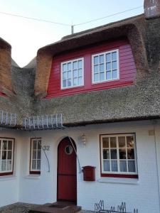 een huis met een rieten dak en een rode deur bij Hochstieg 32, Gonska, Haushälfte in Nieblum