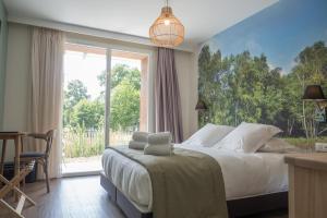 a bedroom with a bed and a large window at Hôtel et Cottages Domaine Du Marquenterre in Saint-Quentin-en-Tourmont