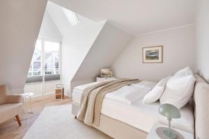 a white bedroom with a bed and a chair at Altstadt Hüs in Wyk auf Föhr
