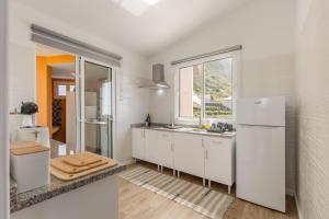a white kitchen with a refrigerator and a window at Coastal São Vicente Mountain & Sea View Hideaway with Free Parking in São Vicente