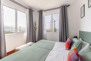 a bedroom with a bed and two windows at Coastal São Vicente Mountain & Sea View Hideaway with Free Parking in São Vicente