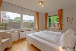 a bedroom with a bed and a chair and two windows at Pidder Lyng 2 EG in Wyk auf Föhr