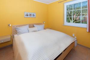 a bedroom with a bed with yellow walls and a window at Ferienhaus Satelsrönne 23 - Wattlaeufer in Duhnen