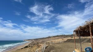 Blick auf einen Strand mit Meer und einer Strohhütte in der Unterkunft Bel appartement centre Asilah proche de la mer in Aïn Harrouda
