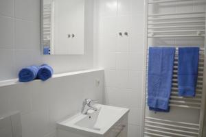 a white bathroom with a sink and blue towels at Ferienresidenz Chiemseestrand - Apartment 32 in Chieming