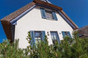 a white house with blue shutters and trees at Dünenbraut in Glowe